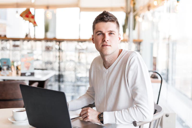 Il riuscito giovane uomo di affari in una camicia bianca con un computer moderno si siede in un caffè Tipo fresco delle free lanc