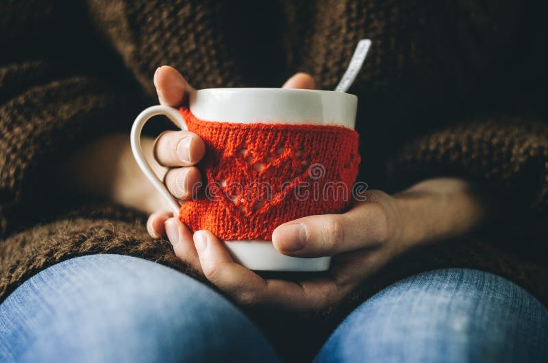 Il rosso ha tricottato la tazza di lana con il modello del cuore in mani femminili immagini stock Il rosso ha tricottato la tazza di lana con il modello del cuore in mani femminili immagini stock