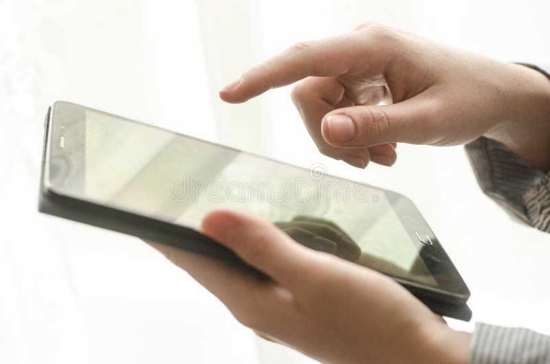 Women`s hands are holding a tablet against the window. Women`s hands are holding a tablet against the window