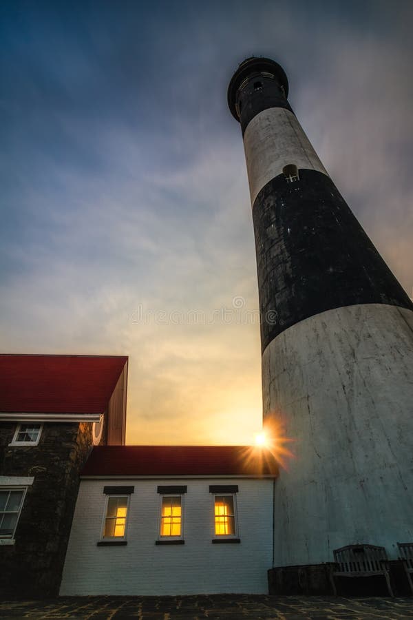 The sun setting behind a lighthouse as golden light shines through its windows. Sun burst and rays - Fire Island New York. The sun setting behind a lighthouse as golden light shines through its windows. Sun burst and rays - Fire Island New York