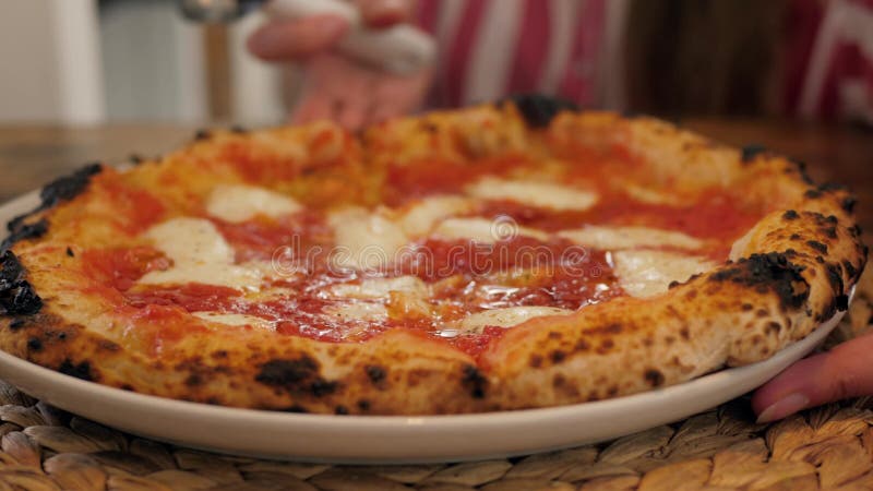 Il taglio del cuoco unico nella pizzeria prepara una pizza e la decora con il pepe ed il basilico del parmigiano