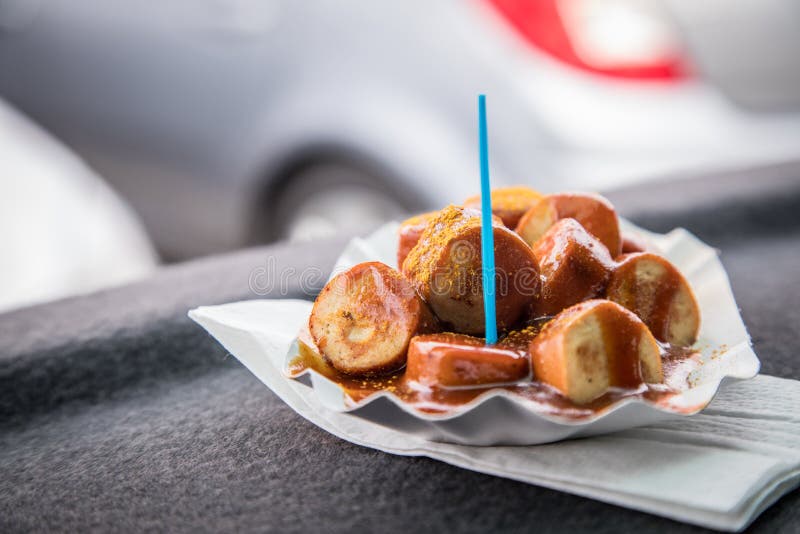 Il tipico piatto tedesco di Currywurst viene grigliato e affettato salsiccia con ketchup al curry su un piatto di carta in macchi fotografia stock Il tipico piatto tedesco di Currywurst viene grigliato e affettato salsiccia con ketchup al curry su un piatto di carta in macchi fotografia stock