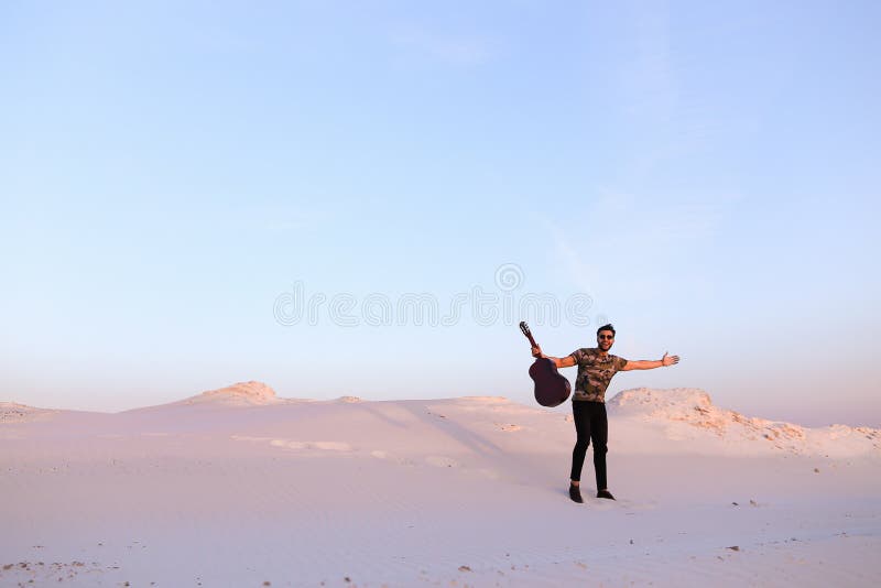 Il tipo arabo va ispirato da bellezza del deserto e gioca lo stri della chitarra immagine stock Il tipo arabo va ispirato da bellezza del deserto e gioca lo stri della chitarra immagine stock