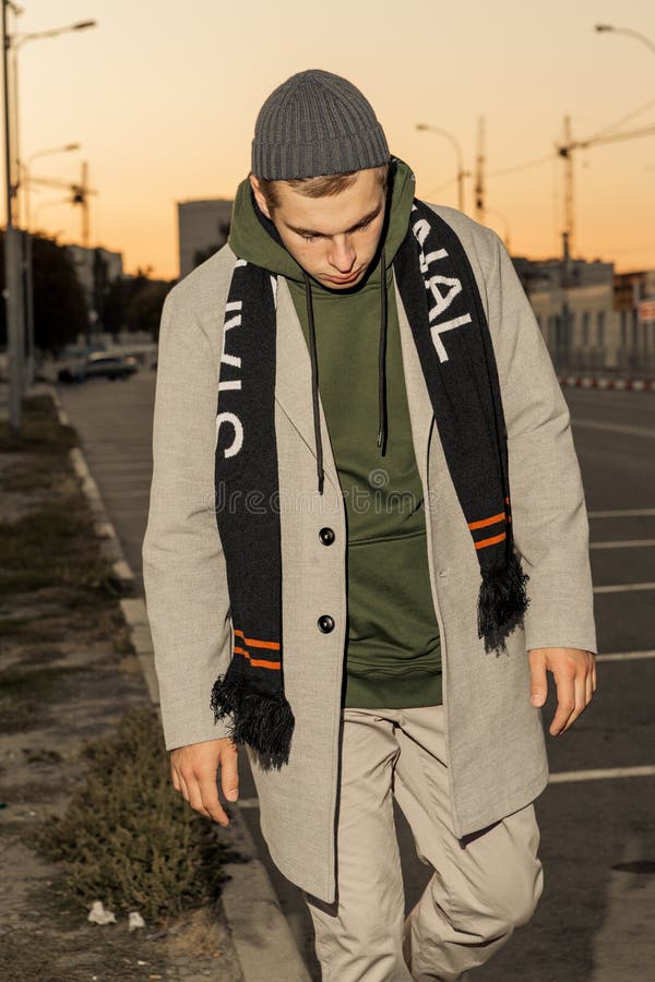 Il tipo bello in vestiti alla moda cammina su una via della città al tramonto immagini stock