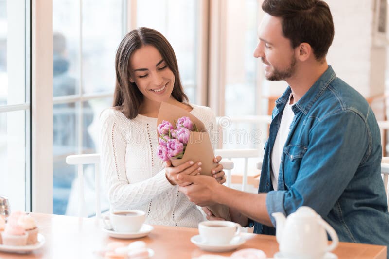 Il tipo dà i fiori alla ragazza nel caffè fotografie stock libere da diritti Il tipo dà i fiori alla ragazza nel caffè fotografie stock libere da diritti