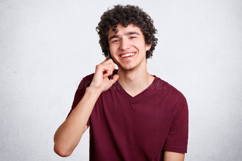 Il tipo felice dei pantaloni a vita bassa o dell'adolescente, parla tramite telefono cellulare con il migliore amico, ha deliziat fotografia stock libera da diritti Il tipo felice dei pantaloni a vita bassa o dell'adolescente, parla tramite telefono cellulare con il migliore amico, ha deliziat fotografia stock libera da diritti