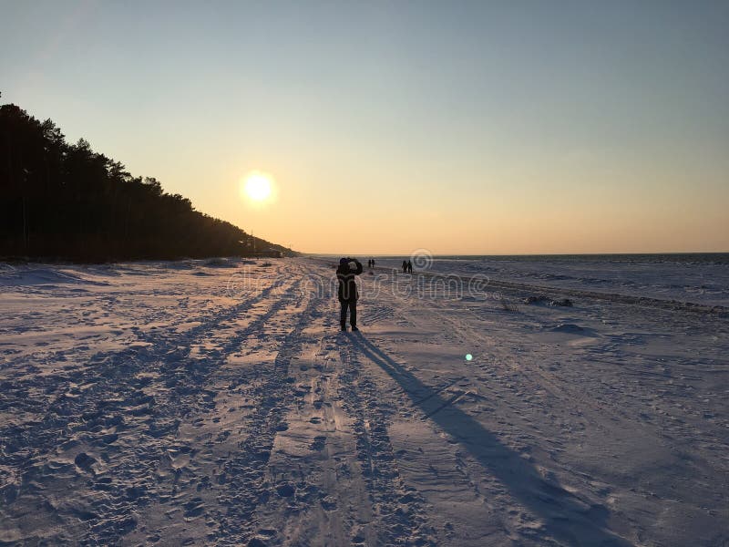 Il tramonto su una serata gelida e una ragazza su una passeggiata lo fotografa Jurmala, Lettonia, 3 gennaio 2018 immagini stock Il tramonto su una serata gelida e una ragazza su una passeggiata lo fotografa Jurmala, Lettonia, 3 gennaio 2018 immagini stock