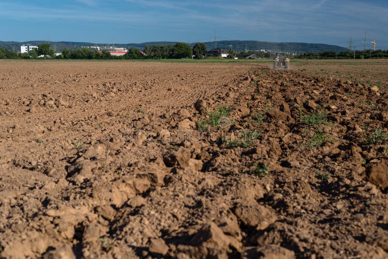 Il trattore tira l'aratro ed il campo arato un giorno di estate soleggiato con un bello cielo blu nei precedenti immagine stock Il trattore tira l'aratro ed il campo arato un giorno di estate soleggiato con un bello cielo blu nei precedenti immagine stock