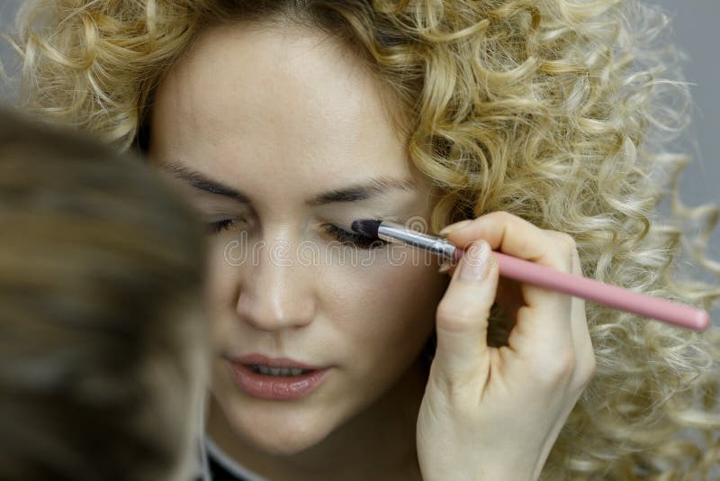 Il truccatore che fa il professionista compone della giovane donna immagine stock Il truccatore che fa il professionista compone della giovane donna immagine stock