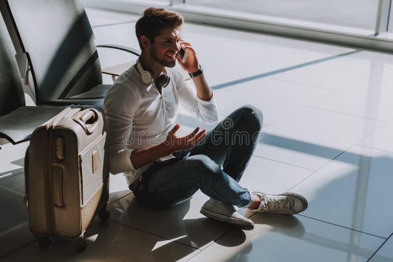 Il turista allegro sta parlando sul telefono all'aeroporto immagini stock Il turista allegro sta parlando sul telefono all'aeroporto immagini stock