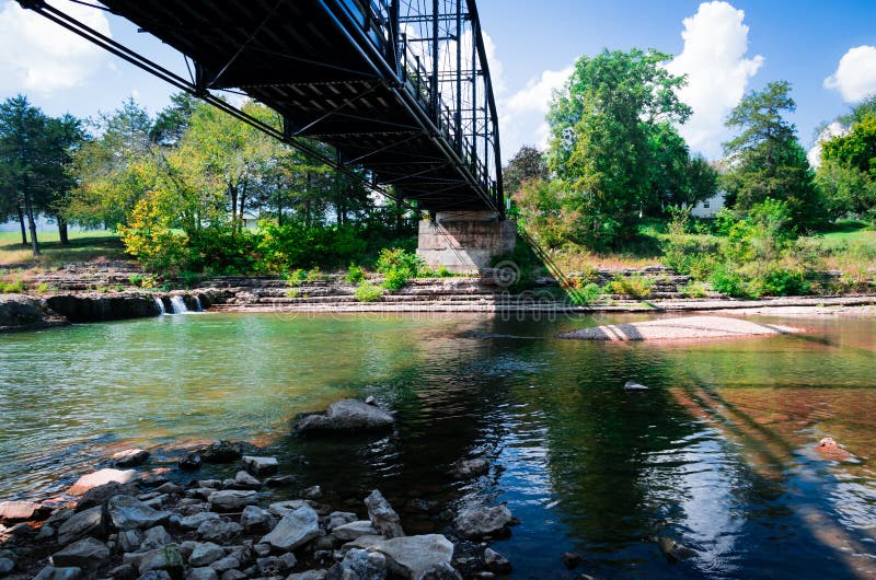 Il vecchio ponte getta le ombre variopinte sulle rocce nel fiume qui sotto fotografia stock Il vecchio ponte getta le ombre variopinte sulle rocce nel fiume qui sotto fotografia stock