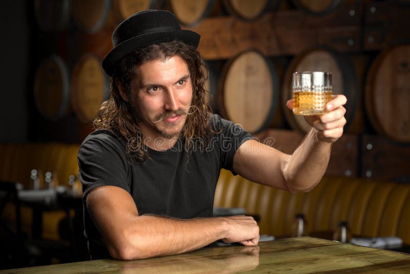 Il vetro del whiskey incoraggia il bourbon bevente dell'uomo alla moda ad una barra del ristorante della distilleria del whiskey fotografie stock Il vetro del whiskey incoraggia il bourbon bevente dell'uomo alla moda ad una barra del ristorante della distilleria del whiskey fotografie stock