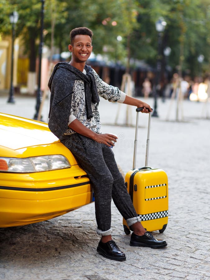 Il viaggiatore bello del giovane con bagaglio e foggia a coppa un caff? messo su un taxi giallo del cappuccio dall'aeroporto Colp fotografia stock libera da diritti Il viaggiatore bello del giovane con bagaglio e foggia a coppa un caff? messo su un taxi giallo del cappuccio dall'aeroporto Colp fotografia stock libera da diritti