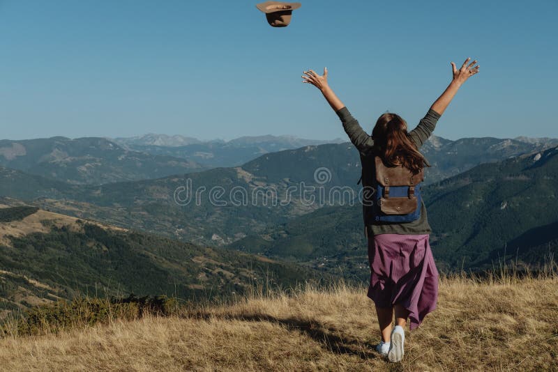 Il viaggiatore posteriore della donna lancia un cappello contro lo sfondo della m. fotografia stock libera da diritti Il viaggiatore posteriore della donna lancia un cappello contro lo sfondo della m. fotografia stock libera da diritti