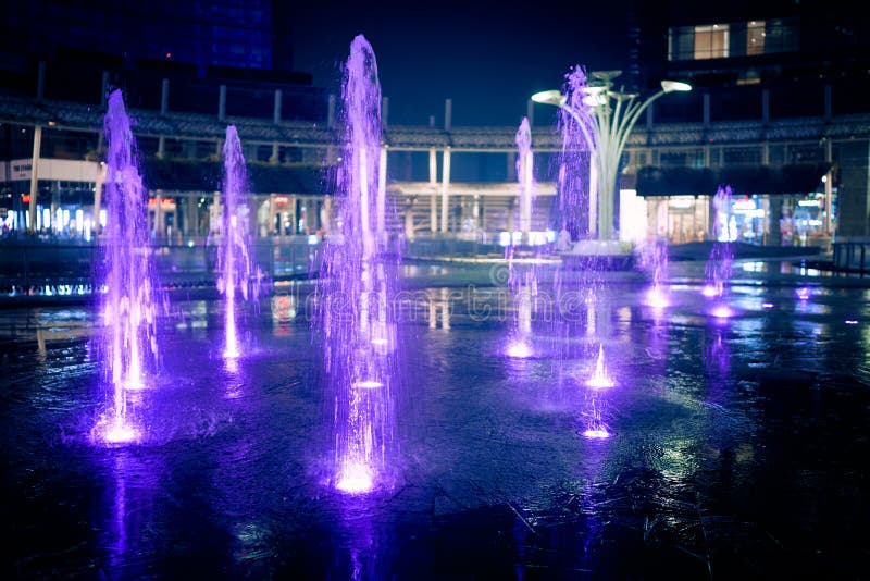 Illuminated splashing water fountains in Gae Aulenti square surrounded by modern skyscrapers. Porta Garibaldi district