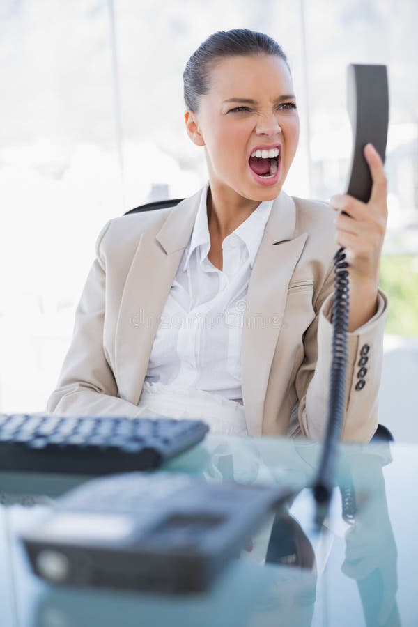 Angry businesswoman screaming at her phone in bright office. Angry businesswoman screaming at her phone in bright office