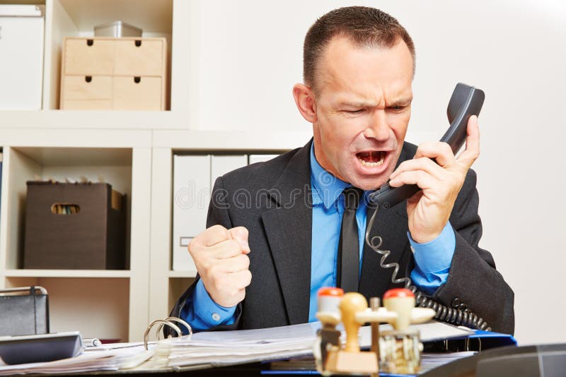 Angry business man screaming at phone in his office. Angry business man screaming at phone in his office