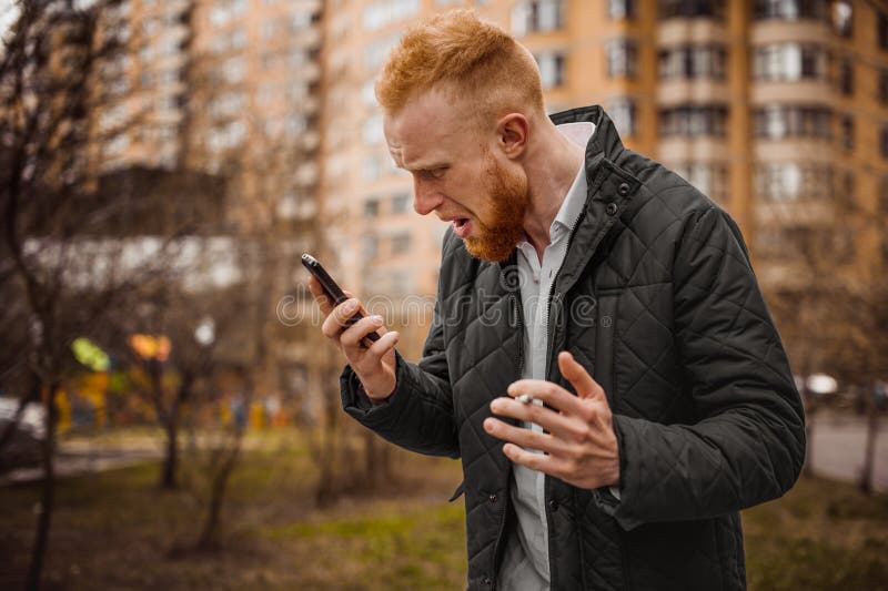 Angry ginger man screaming on phone outdoor. Angry ginger man screaming on phone outdoor