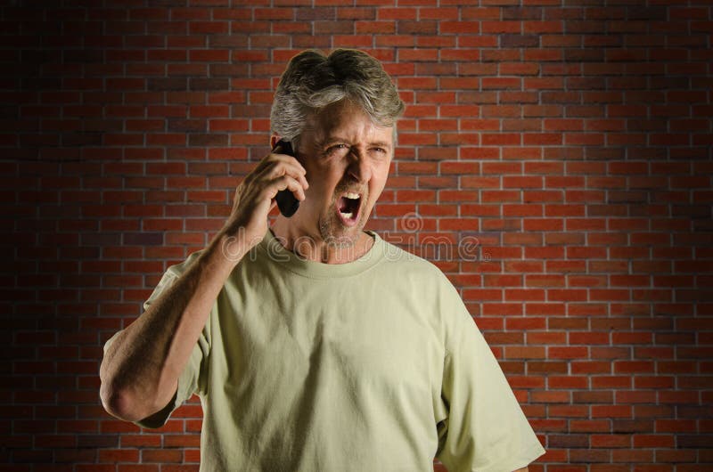 Angry screaming yelling man on his cell phone in a back alley with a brick wall in the background. Angry screaming yelling man on his cell phone in a back alley with a brick wall in the background.