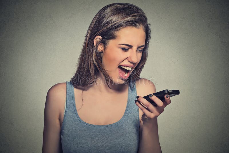 Portrait angry young woman screaming on mobile phone isolated on gray wall background. Negative human emotions feelings. Portrait angry young woman screaming on mobile phone isolated on gray wall background. Negative human emotions feelings