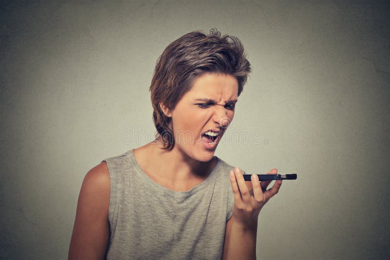 Portrait angry young woman screaming on mobile phone isolated on gray wall background. Negative emotions feelings. Portrait angry young woman screaming on mobile phone isolated on gray wall background. Negative emotions feelings