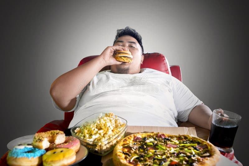 Image of Asian fat man looks greedy while eating junk foods on the sofa. 