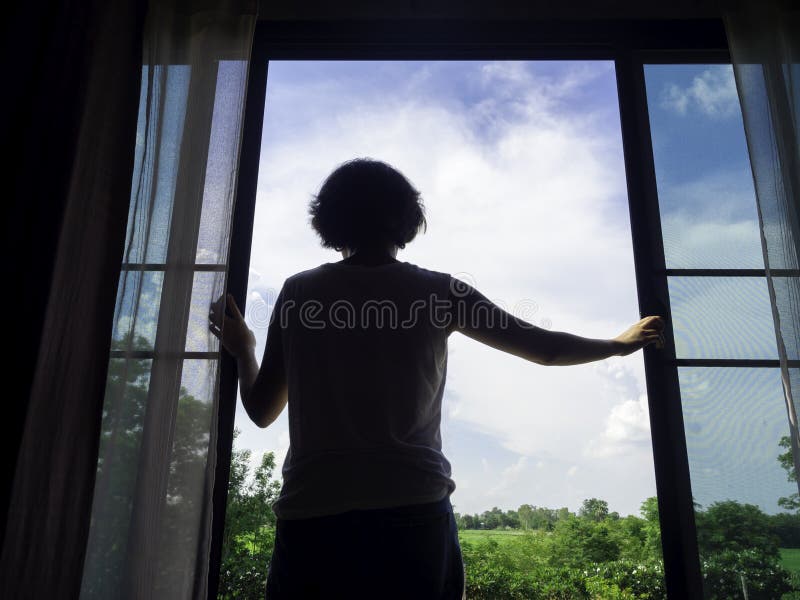 Image of back of woman short hair opening a large glass window in the bedroom on second floor in the house and looking out to green landscape and blue sky on sunny day. Image of back of woman short hair opening a large glass window in the bedroom on second floor in the house and looking out to green landscape and blue sky on sunny day.