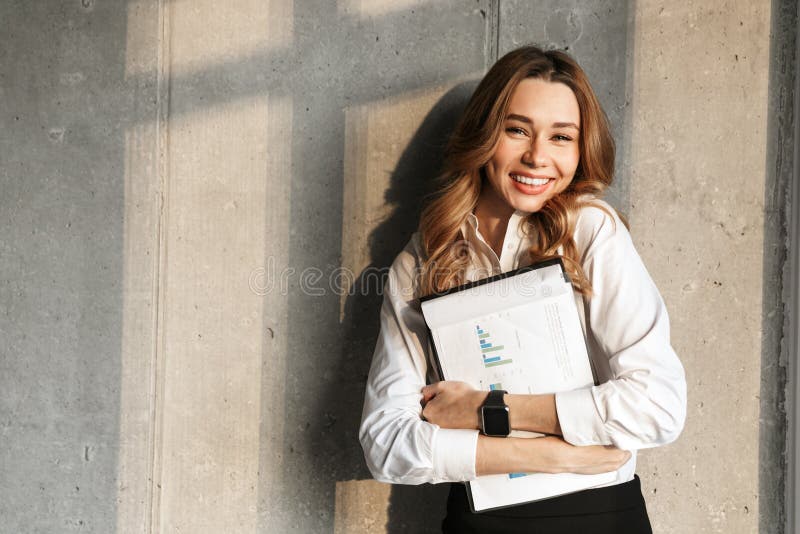 Beautiful young business woman dressed in formal clothes shirt indoors holding documents