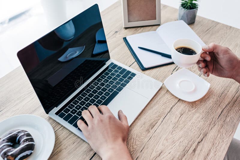 image cultivée de l'homme avec la tasse et le beignet de café à la table avec l'ordinateur portable, manuel, usine mise en pot photo stock image cultivée de l'homme avec la tasse et le beignet de café à la table avec l'ordinateur portable, manuel, usine mise en pot photo stock