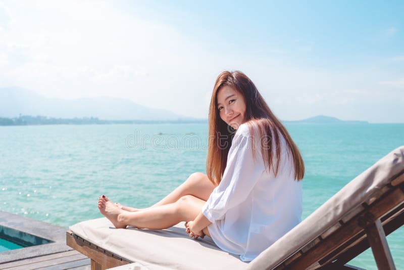 Image de portrait d'une belle femme asiatique heureuse sur la robe blanche se reposant sur le lit du soleil par la mer images libres de droits Image de portrait d'une belle femme asiatique heureuse sur la robe blanche se reposant sur le lit du soleil par la mer images libres de droits