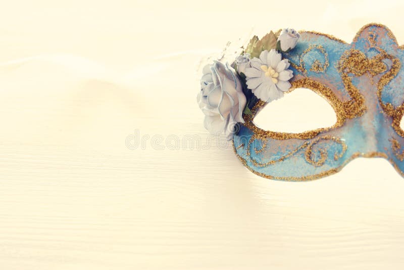 Image of delicate blue elegant venetian mask over wooden white background. Selective focus.