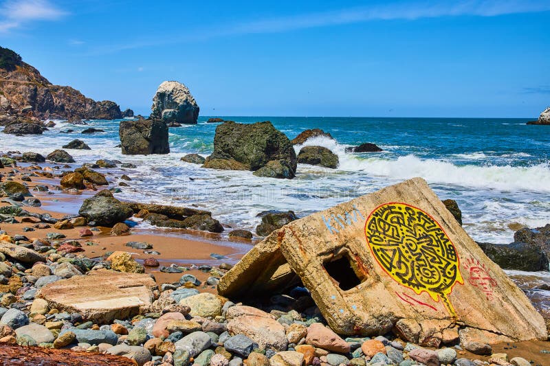 Image of Graffiti on concrete fragment washed on pebbly shore in gorgeous rocky coastline with waves. Concrete fragment stock images, royalty-free photos and pictures