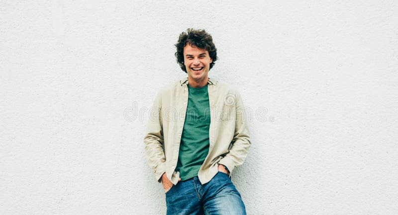 Image of handsome young man with curly hair smiling and posing for advertisement, looking at the camera with copy space for your