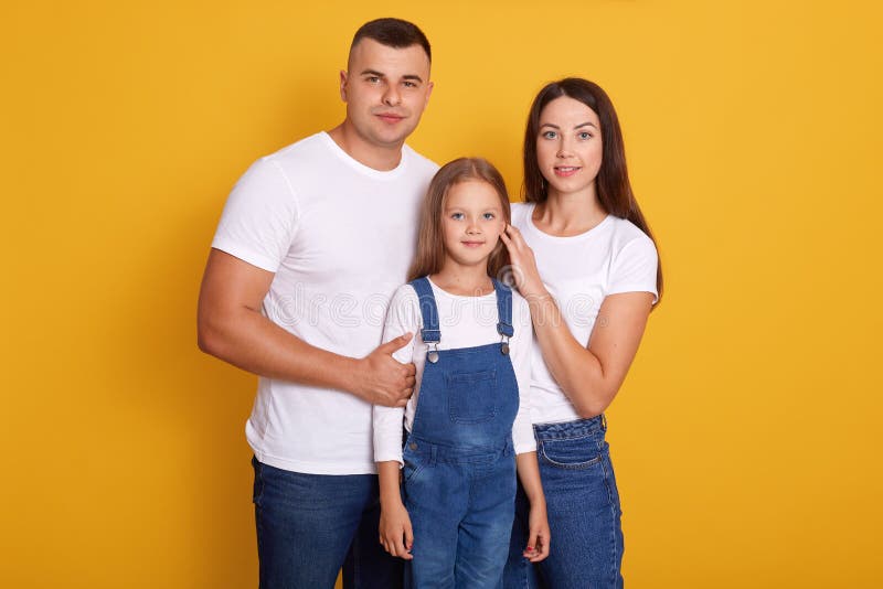 Image of happy Caucasian family pose smiling  over yellow background, parents with cute little daughter enjoy spending together, dress casual outfits, looking at camera. Happyness concept