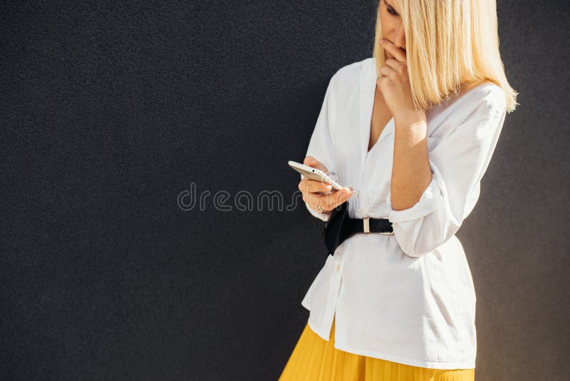 Image horizontale de la lecture femelle blonde sérieuse, message textuel textotant au téléphone portable posant sur le mur gris e photographie stock Image horizontale de la lecture femelle blonde sérieuse, message textuel textotant au téléphone portable posant sur le mur gris e photographie stock
