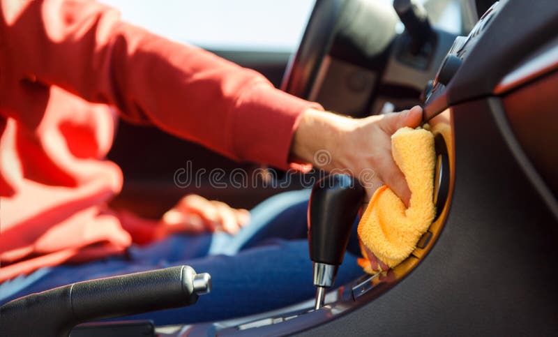 Image of human hand with orange cloth washing car interior, close-up