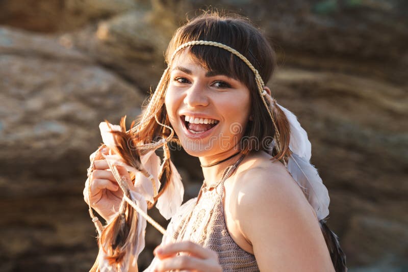 Image of joyful hippy girl wearing feather headband walking by seaside