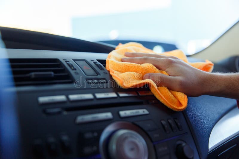 Image of male`s hand with orange rag washing car interior, close-up