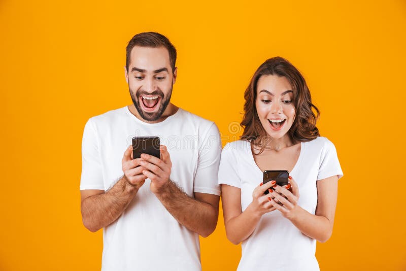 Image of positive couple man and woman smiling while both using mobile phones, isolated over yellow background royalty free stock image Image of positive couple man and woman smiling while both using mobile phones, isolated over yellow background royalty free stock image