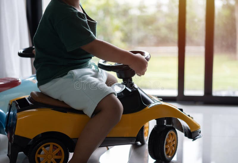 Cropped image of little Asian boy driving children's electric toy car near the door at home. The concept of a happy childhood. Cropped image of little Asian boy driving children's electric toy car near the door at home. The concept of a happy childhood