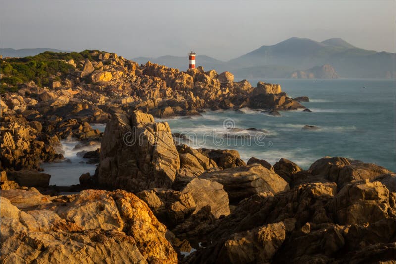 Immagine di un faro rosso e bianco su rocce e massi da un oceano di Tuy, Un Distretto di Phu Yen Provincia, il Vietnam, la mattina presto per gli sfondi.