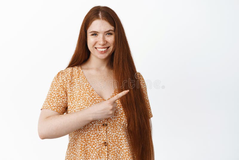 Image of smiling natural redhead girl with long hairstyle, pointing right and looking happy, showing logo or banner