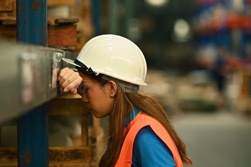Image of tired storehouse worker in hardhat and jacket leaning against metallic rack while having short break royalty free stock images
