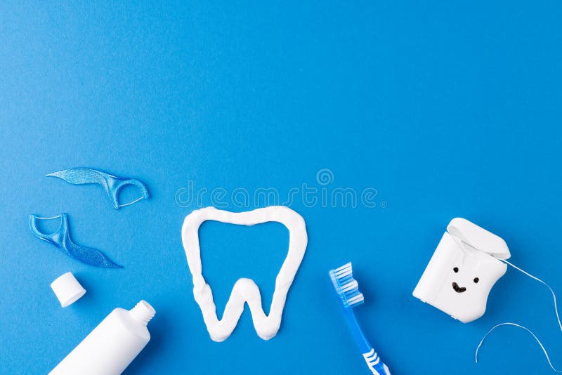 Image of toothbrush, toothpaste, string, liquid and tooth made of paste on blue surface stock images
