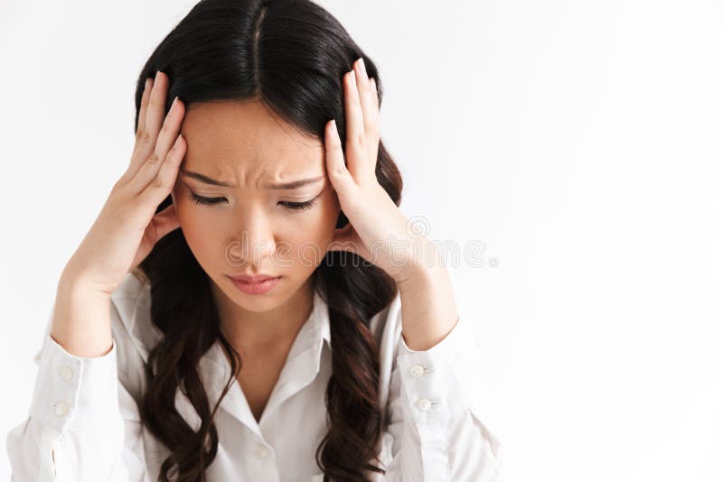 Image of upset or tired asian business woman 20s wearing office clothing sitting at table and grabbing head with hands isolated over white background