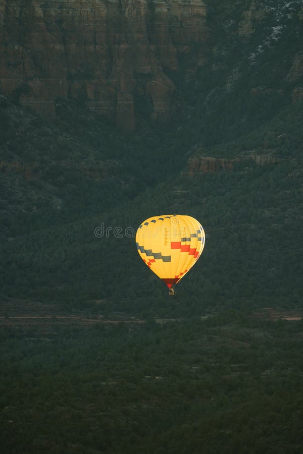 Image verticale du téléphoto de la montgolfière jaune dégageant des flammes sur fond de fond de la vallée sombre au début