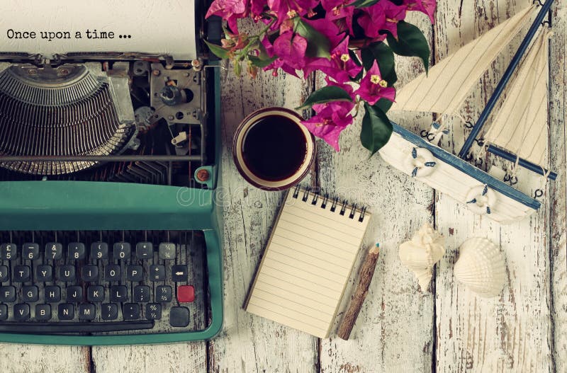 Image of vintage typewriter with phrase once upon a time, blank notebook, cup of coffee and old sailboat