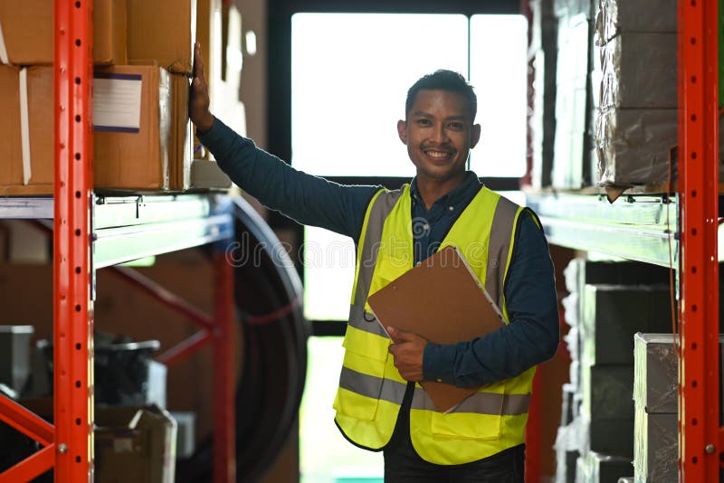 Image of warehouse worker wearing reflective vest holding clipboard standing in retail warehouse stock photography