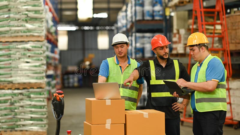 Image of warehouse workers are inspecting stock on laptop while standing aisle between rows of tall shelves full of stock photo