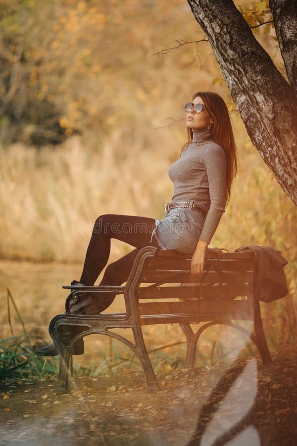 Image of woman in sunglasses sitting on bench in autumn park